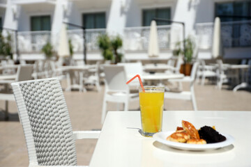 Glass of orange juice with plastic straw on white table in restaurant outdoor lounge zone in sunny weather