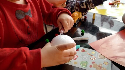Closeup of two boys making handmade Christmas baubles, painting and decorating them with glitter. Winter holidays, family time together, kids with parents celebrating.
