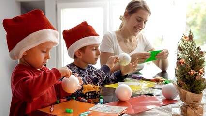 Happy kids with mother cutting out Christmas garlands from colorful paper. Winter holidays, family...