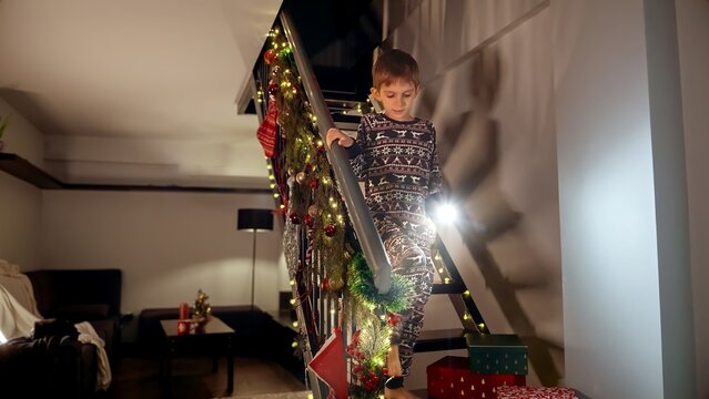 Little boy in pajamas running down the stairs with torch on Christmas night