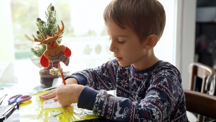 Portrait of thoughtful little boy thinking of what to wish on Christmas while writing letter to...