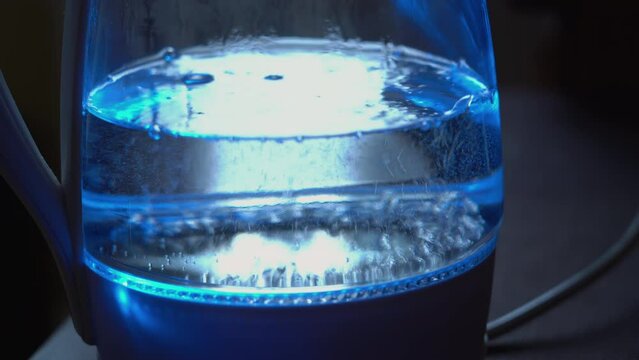 Transparent kettle with boiling water with neon lighting. The concept of a coffee break and the end of the working day.
