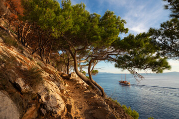 Far view of boat on the sea near the Makarska city, Croatia. Beautiful landscape in Park Osejava near Makarska, Croatia. Gravel path in forest near Adriatic sea.
