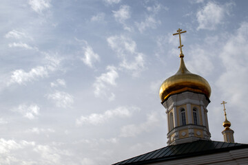 The dome of the temple with a cross is gilded. The Orthodox Cross on the Dome of the Christian Church, a view from below. The golden orthodox cross of the temple against the background of the blue sky