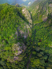 Drone flight above rocky mountain peaks covered with luxuriant and wild beech forests. The valley winds through sharp ravines. Olt river flows in the background. Carpathia, Romania.