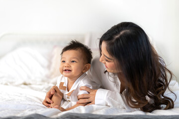 Obraz na płótnie Canvas Portrait of enjoy happy love family asian mother playing with adorable little asian baby.Mom touching with cute son moments good time in a white bedroom.Love of family concept