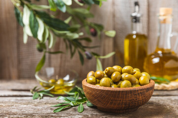 Green olives on a white wooden background. Various types of olives in bowls and olive oil with fresh olive leaves. Copy space. Place for text. Mediterranean food. Vegan.