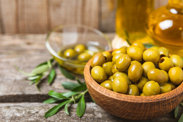 Green olives on a white wooden background. Various types of olives in bowls and olive oil with fresh olive leaves. Copy space. Place for text. Mediterranean food. Vegan.