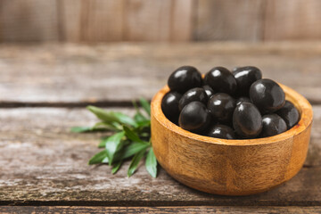 Black olives on a  wooden background. Various types of olives in bowls and olive oil with fresh olive leaves. Copy space. Place for text. Mediterranean food. Vegan.