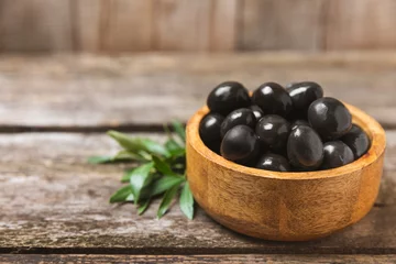 Poster Black olives on a  wooden background. Various types of olives in bowls and olive oil with fresh olive leaves. Copy space. Place for text. Mediterranean food. Vegan. © Avocado_studio