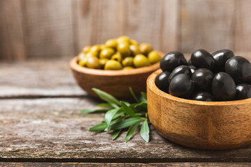 Green and black olives on a white wooden background. Various types of olives in bowls and olive oil with fresh olive leaves. Copy space. Place for text. Mediterranean food. Vegan.