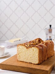 Butter brioche bread sprinkled with almond petals on a wooden board on a light concrete background. Wheat bread recipes.