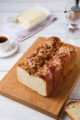Butter brioche bread sprinkled with almond petals on a wooden board on a light concrete background. Wheat bread recipes.