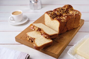 Butter brioche bread sprinkled with almond petals on a wooden board on a light concrete background. Wheat bread recipes.