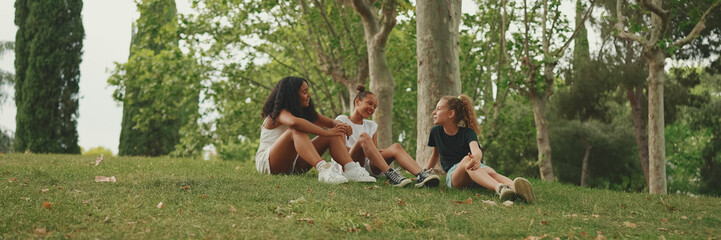 Three girls friends pre-teenage sit on the grass in the park and emotionally talking. Three...