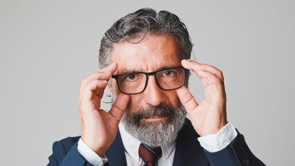 Close-up of businessman putting on glasses and looking at the camera, isolated on gray background