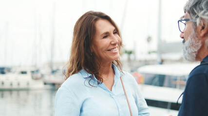Lovely elderly woman standing in the port and talking to her boyfriend on the yacht background