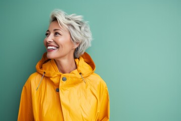 Fototapeta premium Portrait of a cheerful woman in her 50s wearing a vibrant raincoat against a solid pastel color wall. AI Generation