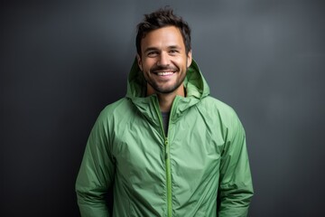 Fototapeta premium Portrait of a smiling man in his 30s wearing a lightweight packable anorak against a bare monochromatic room. AI Generation