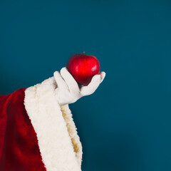 Santa's hand in a white glove holds a red apple. Healthy eating concept.