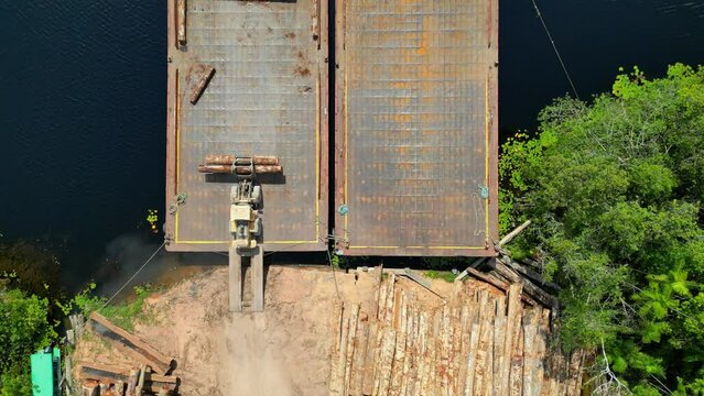 Aerial drone view of a riverbank barge being laden with timber woods harvested from the heart of the Amazon rainforest