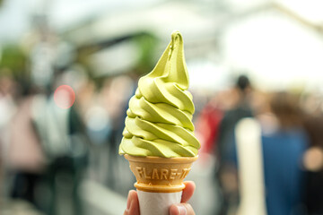 Matcha green tea soft serve ice-cream in waffle cone which is holded on person hand. Ready to...