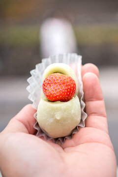 A strawberry green tea mochi, one of the famous Japanese dessert food, is holding on the person hand. Sweet food object photo. Selective focus.