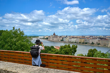 A tourist taking a photo of the Hungarian parliament building while sightseeing on a warm and sunny...