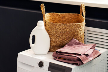 White bottle with laundry detergent, basket with clothes, towel  standing on watching machine in...