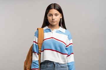 Focused teen student girl with backpack on shoulder isolated studio background. Serious unsmiling joyless young teenager schoolgirl looking at camera. Beginning of academic year, admission to college