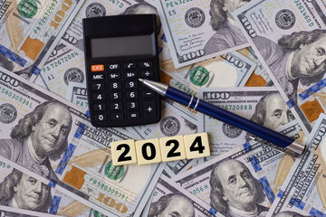 Inscription 2024, calculator, and pen lying on a background composed of hundred dollar bills,...