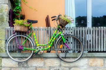 Multi-colored bicycle with baskets of flowers hanging on a wooden fence of a residential building.