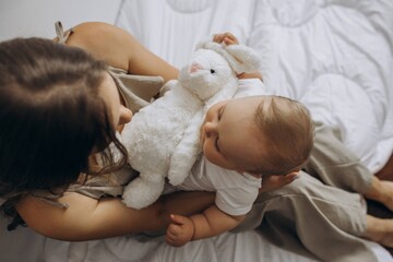 mother holding her baby son on hands and her knees and a white rabbit toy fluffy