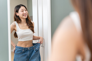 Happy Young women look themselves when wearing old pants before weight loss in the mirror and are proud of her diet results.