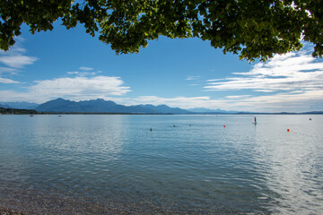 Summer view across the Chiemsee in the Bavarian Alps, with swimmers and paddle boarders enjoying recreational activities in the water