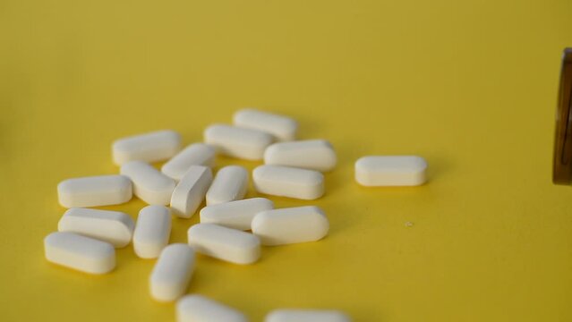 White medical pills or tablets with a bottle on a yellow background. Side view of macro with copy space