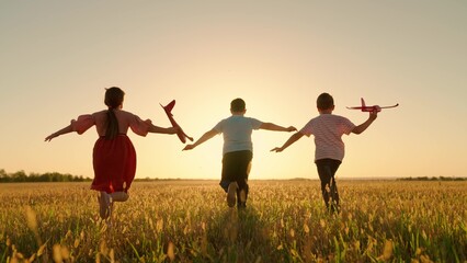 Happy children run with toy plane across field at sunset. Boy, girl wants to become pilot, an...