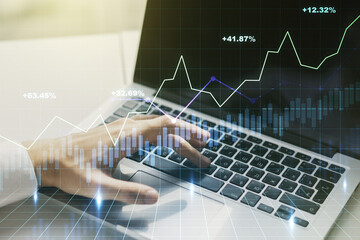 Abstract creative financial graph with hand typing on laptop on background, financial and trading concept. Multiexposure