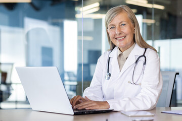 Portrait of mature experienced female doctor, gray-haired senior woman in white medical coat...