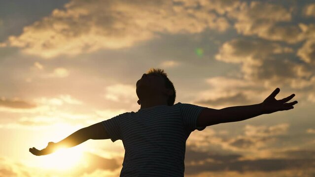 Child boy plays in park against sky, Happy family, Child raised his hands to sky in park at sunset, true faith. Little boy prays against background of sky and sun. Religion and god, childhood dreams.