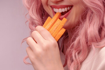 Carrots cut into strips in woman hand. Woman with pink curly hair is eating carrot.