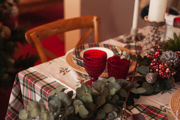 christmas table setting in red color palette with checkered classic tablecloth with green garland