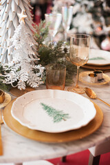 christmas table setting in gold green color palette with view on xmas tree and golden cutlery. Festive plate closeup.