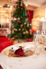 elegant Christmas table setting with trendy plates, candles and golden cutlery, gold accessories with xmas tree view