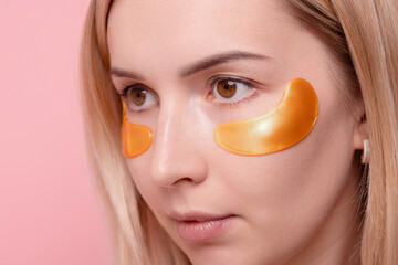Portrait of pretty girl applying golden collagen patches under her eyes in unusual way. Woman...