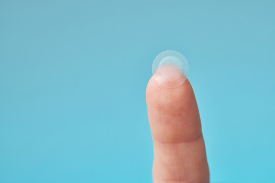 Close-up round acne patch on finger on blue background. Acne patches for treatment of pimple and rosacea close-up. Facial rejuvenation cleansing cosmetology