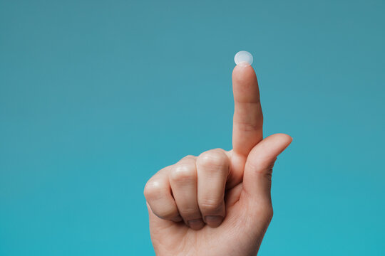 Close-up round acne patch on finger on blue background. Acne patches for treatment of pimple and rosacea close-up. Facial rejuvenation cleansing cosmetology