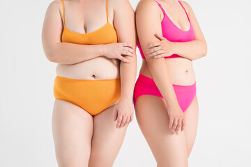 Two overweight women with fat flabby bellies, legs, hands and hips on gray background, plastic surgery and body positive concept