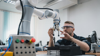 Student engineer Assembling Robotic Arm with computer in Technology Workshop. Service Engineer Holding Robot Controller and Checking Robotic Arm Welding Hardware.