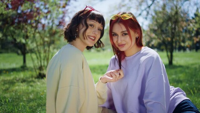 In front of the camera charismatic and Bea ladies posing in front of the camera in the middle of the park they are sitting down on the grass together